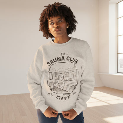 Person wearing a gray sweatshirt with 'The Sauna Club' hand drawn design 